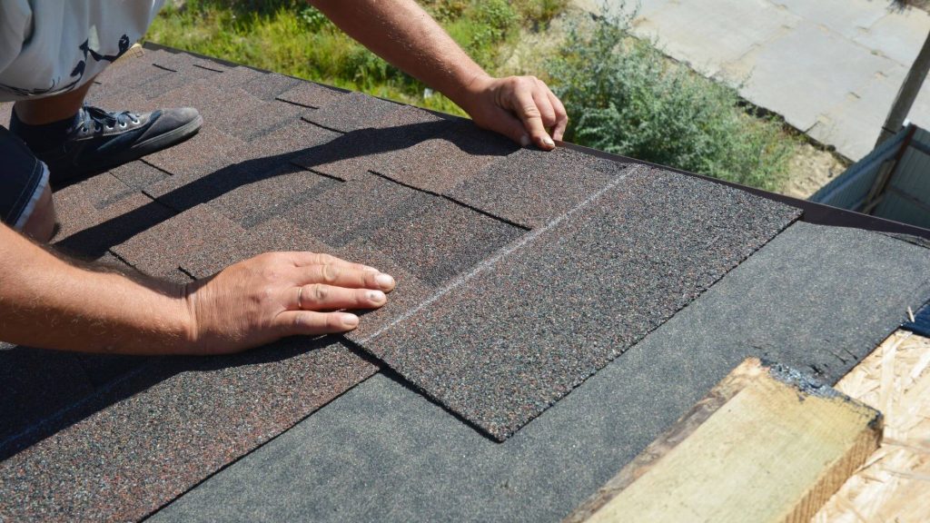 close up of a man's hands lining up new shingles on a roof